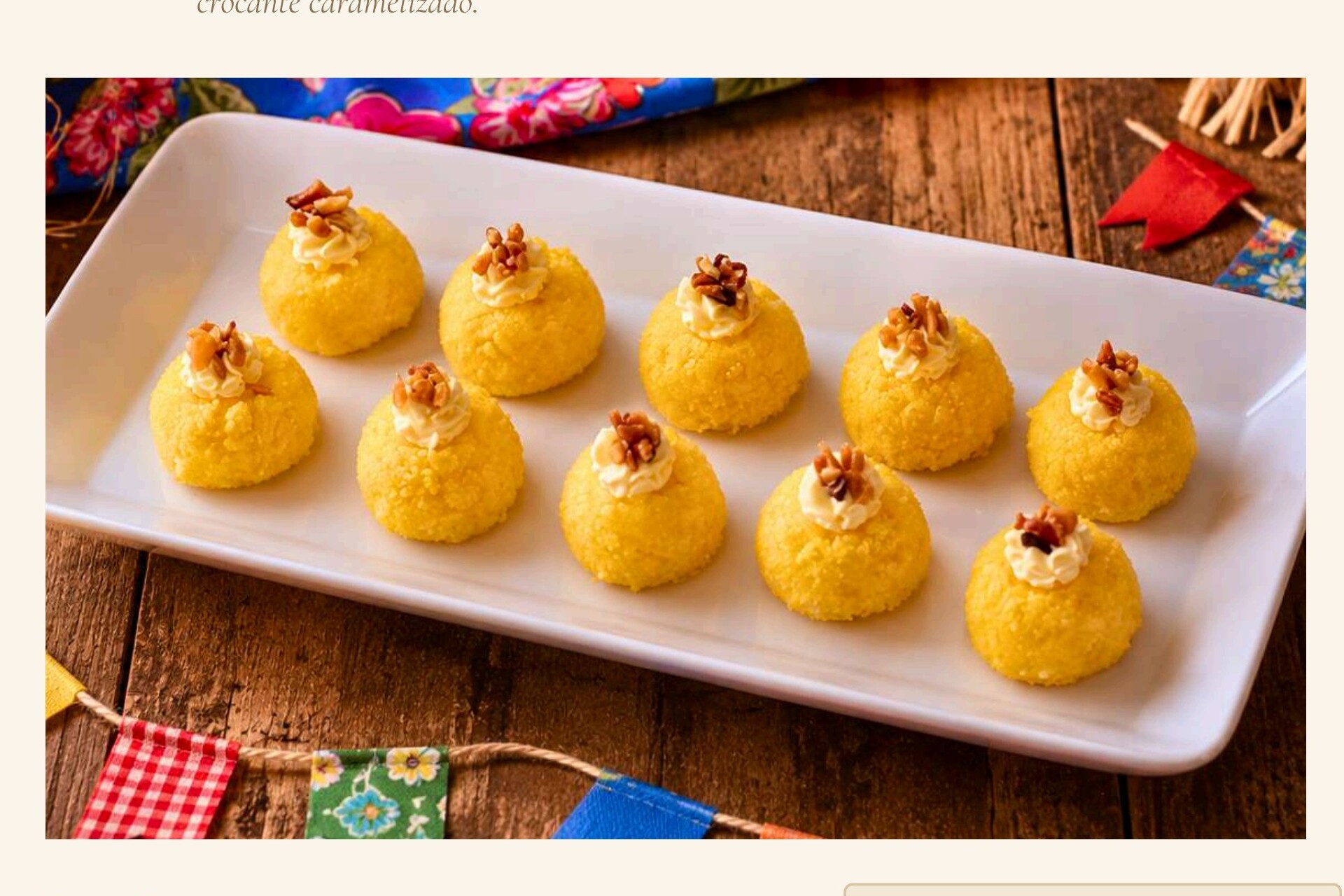 Brigadeiros amarelos de cuscuz em bandeja branca com bandeirinhas juninas ao fundo.