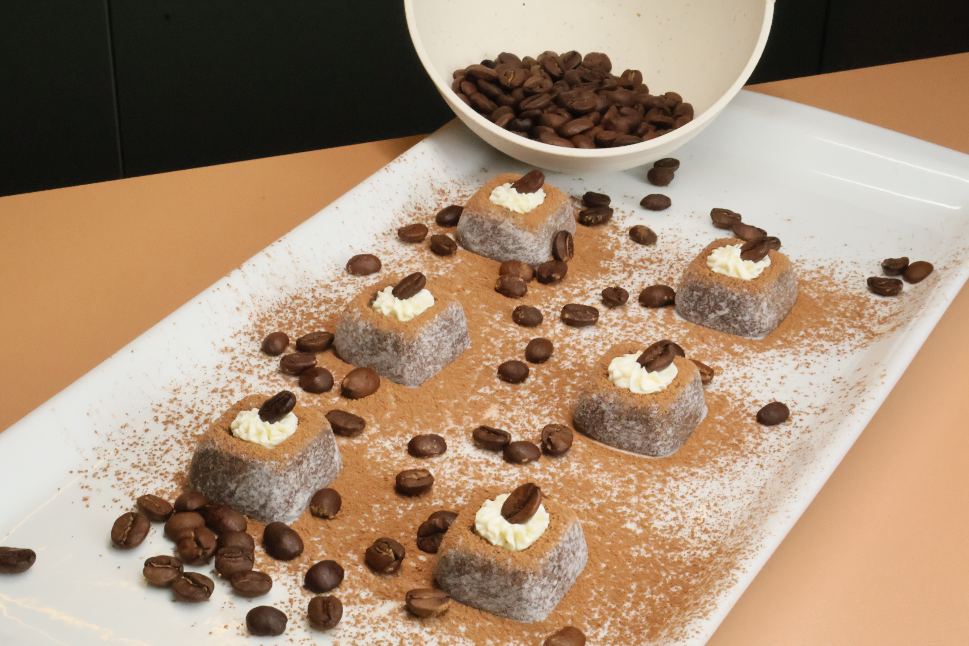 Brigadeiros de cappuccino polvilhados com cacau, cream cheese e grãos de café sobre prato branco.