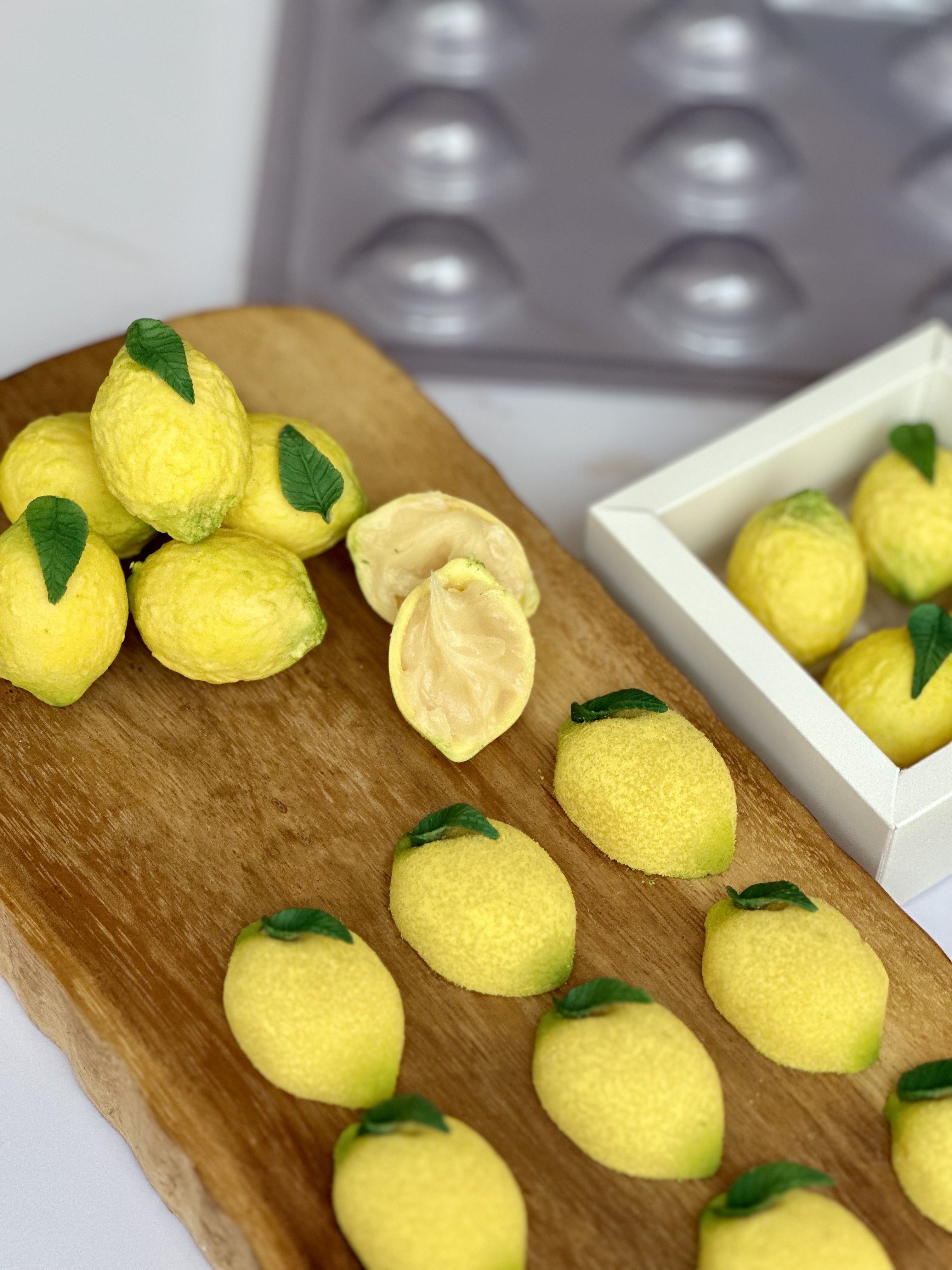 Bombons em formato de limão siciliano amarelos com folhas comestíveis sobre tábua de madeira.