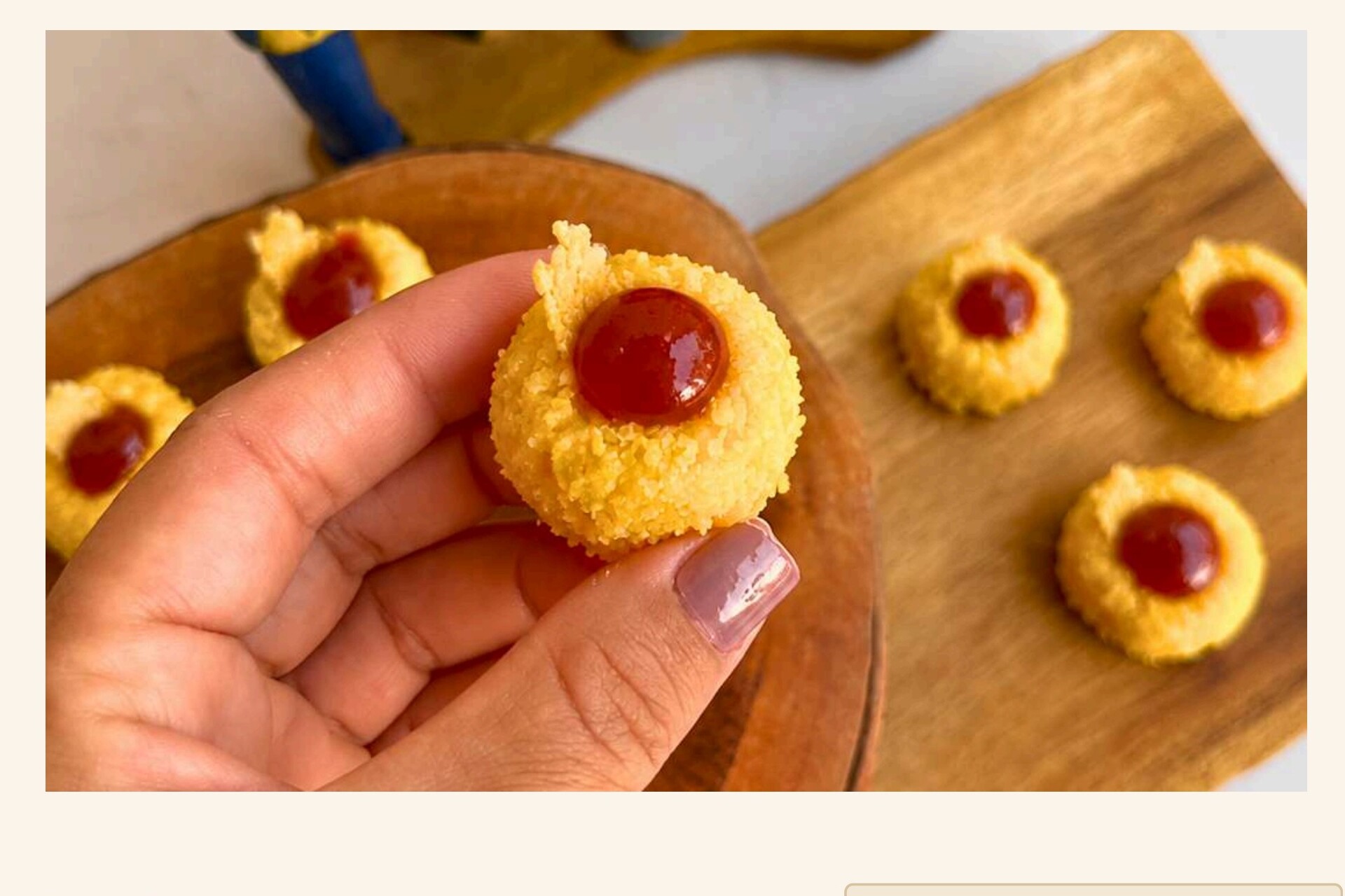Brigadeiro de cuscuz com geleia de goiabada segurado pela mão sobre tábua de madeira.